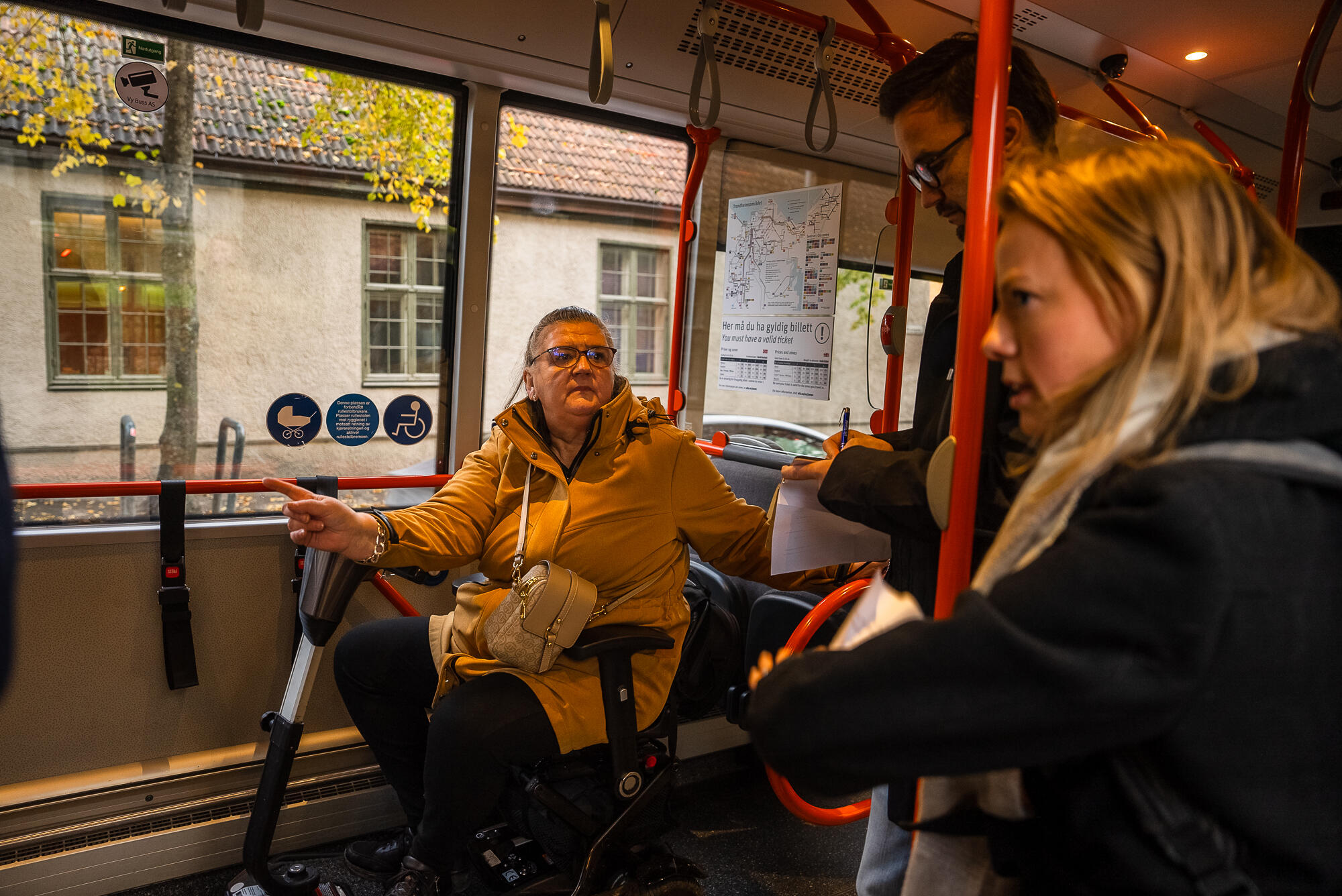 En kvinne i rullestol peker og forklarer om bord i en buss