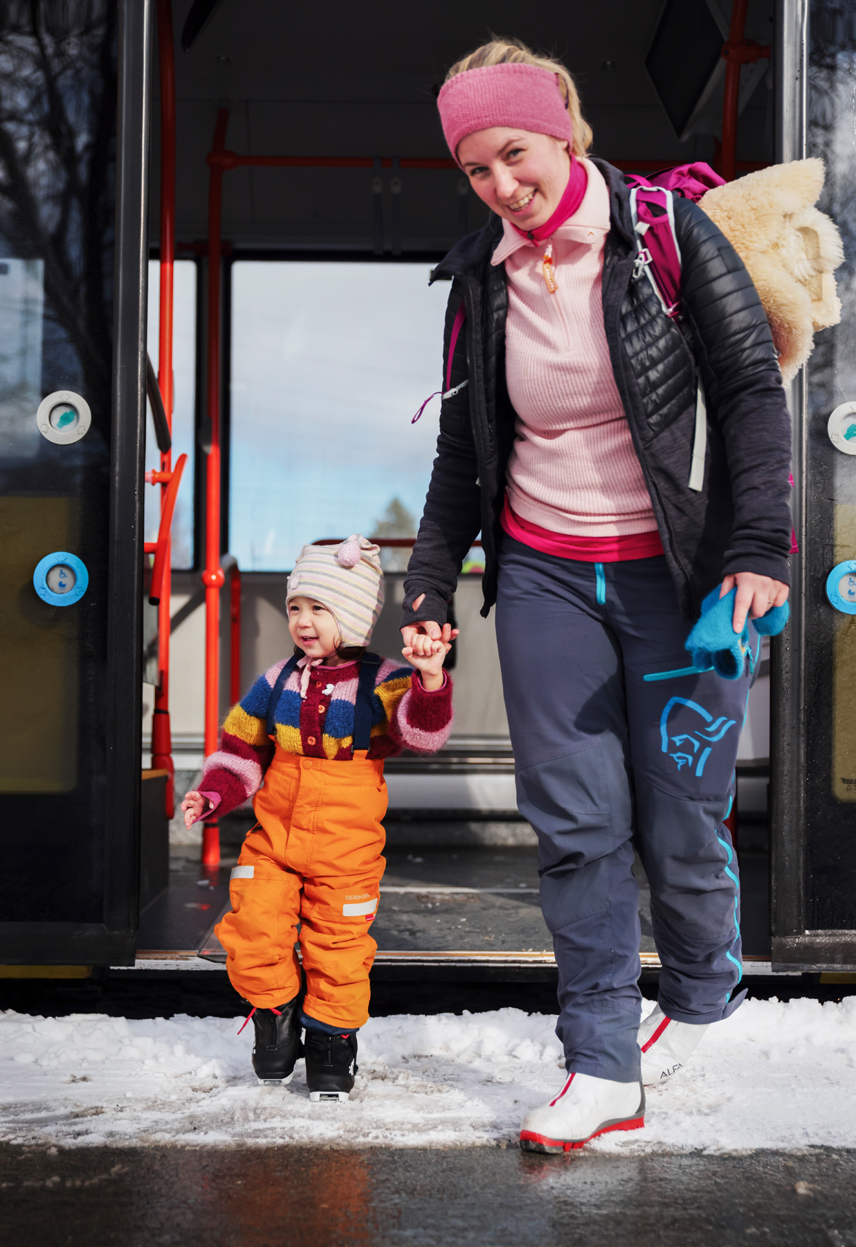 Mor og barn på vei ut av bussen med skiutstyr